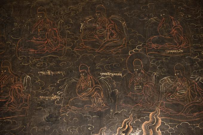 Covering the walls, the seated robed figures, picked out in a delicate white line from the deep black ground of the walls are the principle lineage holders associated with Sakyapa tantra related to Gur Gönpo. the principle lineage holders of the sakya tradition