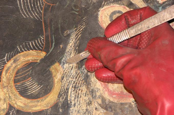 The first step in the restoration process was to clean the walls of accumulated deposits of smoke and dirt. The restorers then carefully removed coarse plasters of local clay that had been used in earlier restorations with a scalpel. cleaning a section of a representation of Brahmarupa Mahakala